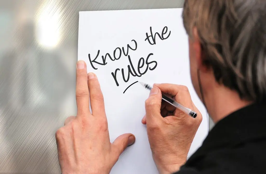 A man writing on paper that says " know the rules ".